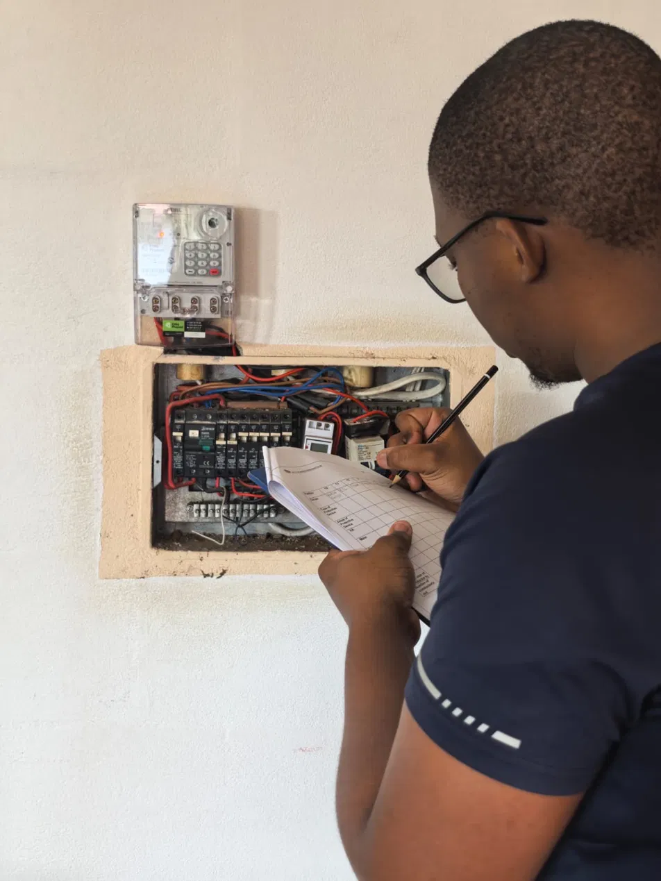Gridsmith electrician writing a COC checklist next to a prepaid meter and open DB board